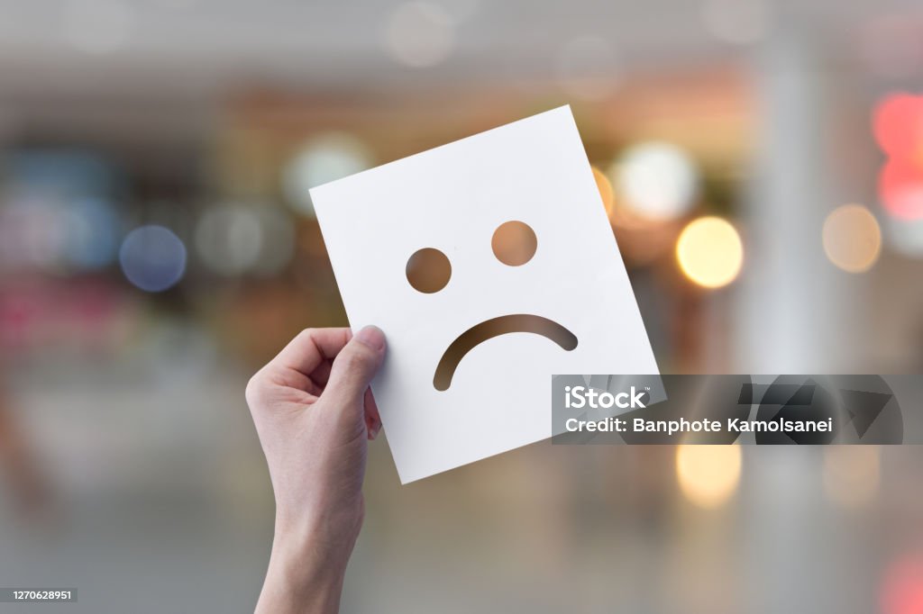 Hand holding white paper with smiley face emoticons (perforated paper) over light bokeh background. Hand holding white paper with unhappy face emoticons (perforated paper) over light bokeh background. Feedback Stock Photo