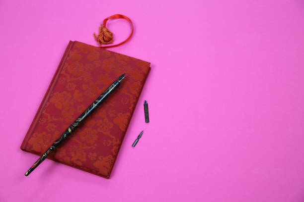 istock View on isolated notebook with red floral pattern cover, old feather ink pen and bookmark on pink background with copy space for text 1270629622