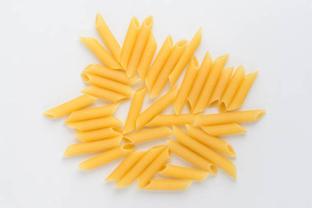 Dried penne Italian pasta displayed randomly on a white table, ready to be cooked, isolated on table background, with top view