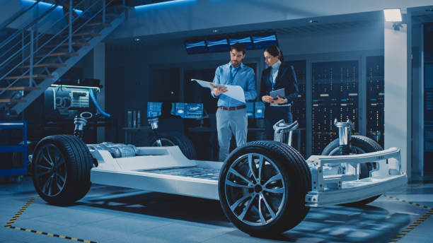 istock Auto Industry Design Facility: Male Chief Engineer Shows Car Blueprints Female Software Design and Integration Engineer. Electric Vehicle Platform Chassis Concept Has Wheels, Engine and Battery 1270630025