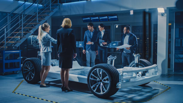 istock Diverse Team of Automobile Design Engineers Introducing Futuristic Autonomous Electric Car Platform Chassis to a Group of Investors and Businesspeople. Vehicle Frame with Wheels, Engine and Battery 1270630027