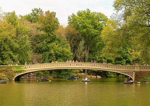 New York City, USA - October 7, 2019: The Bow Bridge in Central Park. Pepole walking across the bridge or looking in the lake. Rowing boats are under the bridge.