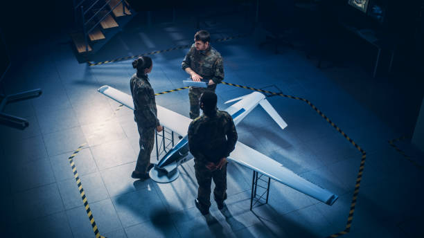 istock Army Aerospace Engineers Work On Unmanned Aerial Vehicle / Drone. Uniformed Aviation Experts Talk, Using Laptop. Industrial Facility with Surveillance, Warfare Tactics, Attack Machine. Elevated Shot 1270630210