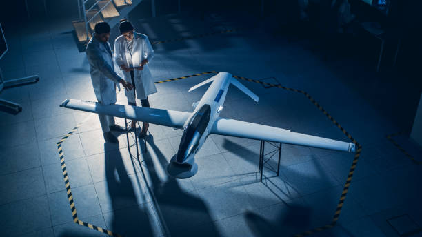 istock Two Aerospace Engineers Work On Unmanned Aerial Vehicle / Drone Prototype. Aviation Scientists in White Coats Talking, Using Tablet Computer. Industrial Laboratory with Surveillance Military Aircraft 1270630217