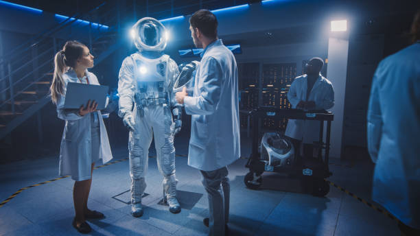 istock Team of Aerospace Scientists and Engineers Wearing White Coats have Discussion, Use Computers, Construct Astronaut Helmet for New Space Suit Adapted for Exploration and Travel. 1270630224