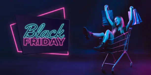 Photo of Portrait of young woman in neon light on dark backgound. The human emotions, black friday, cyber monday, purchases, sales, finance concept. Neoned lettering.