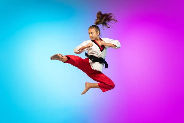 Karate, taekwondo girl with black belt isolated on gradient background in neon light In jump. Karate, taekwondo girl with black belt isolated on gradient background in neon light. Little caucasian model, sport kid training in motion and action. Sport, movement, childhood concept. martial arts stock pictures, royalty-free photos & images