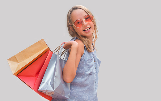 Child with glasses on a gray background.  girl holding shopping bags