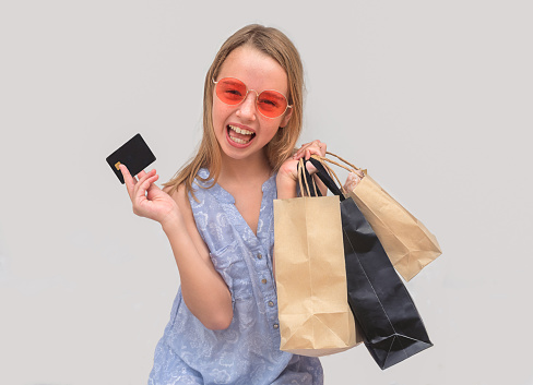 Happy child girl in bright sunglasses with shopping bags and a credit card.