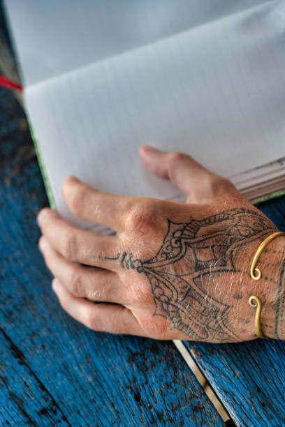 istock Female tattooed hand resting on blank notebook page 1270644027