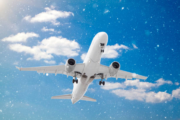 istock white passenger plane has released its landing gear and is landing through falling snow against background of white clouds and blue skies in winter 1270645834