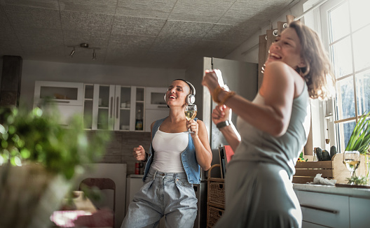 Two girl friends playing guitar in the kitchen near window at home