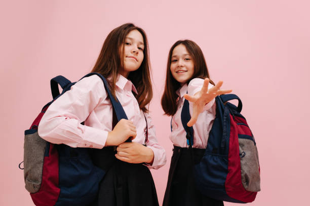istock Cool-looking little twin schoolgirls posing with their backpacks. Low angle 1270646975