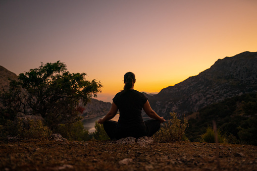 Mature woman meditating in Majorca's landscape with the reservoir in the background, low key photograph