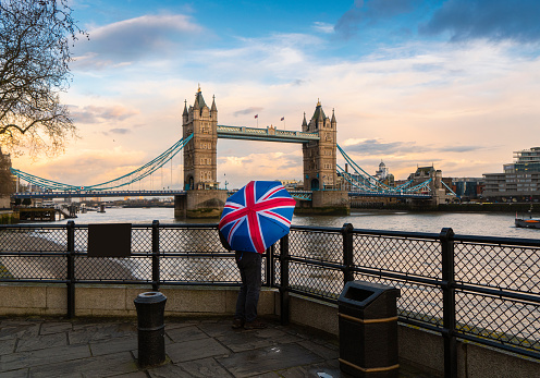 A tourist with a British (Union Jack) flag umbrella watching the sunset over Tower Bridge, London