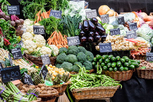 Green organic vegetables in display for sale at a street food market, with names displayed in English, carrots, white asparagus, courgette, aubergine, broccoli, British rhubarb, potatoes, cauliflower, kale, parsnip from a farm