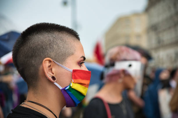 Woman activist wearing rainbow face mask. Warsaw, Poland, June 2020: LGBT supporters protesting on the street with rainbow flags. Portrait of woman activist with rainbow protective face mask transgender protest stock pictures, royalty-free photos & images