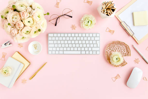 istock Stylized, pink women's home office desk. Workspace with computer, bouquet ranunculus and roses, clipboard on pink background. Flat lay. Top view 1270671283