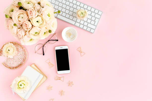 istock Stylized, pink women's home office desk. Workspace with computer, bouquet ranunculus and roses, phone on pink background. Flat lay. Top view 1270673828