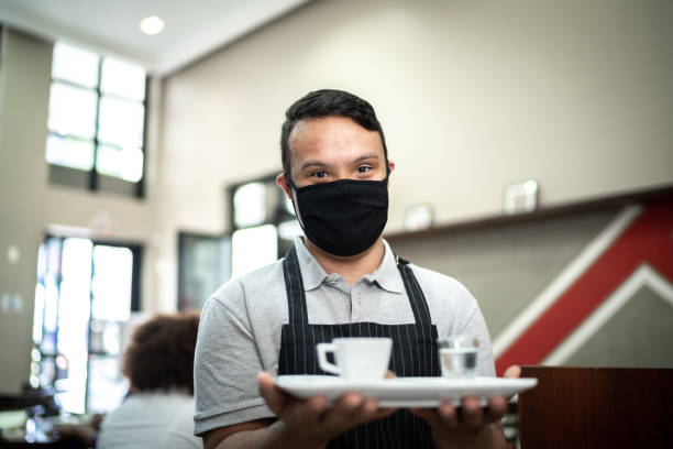 porträtt av en ung servitör bär ansiktsmask och håller en bricka med en kaffemugg - downs syndrome work bildbanksfoton och bilder