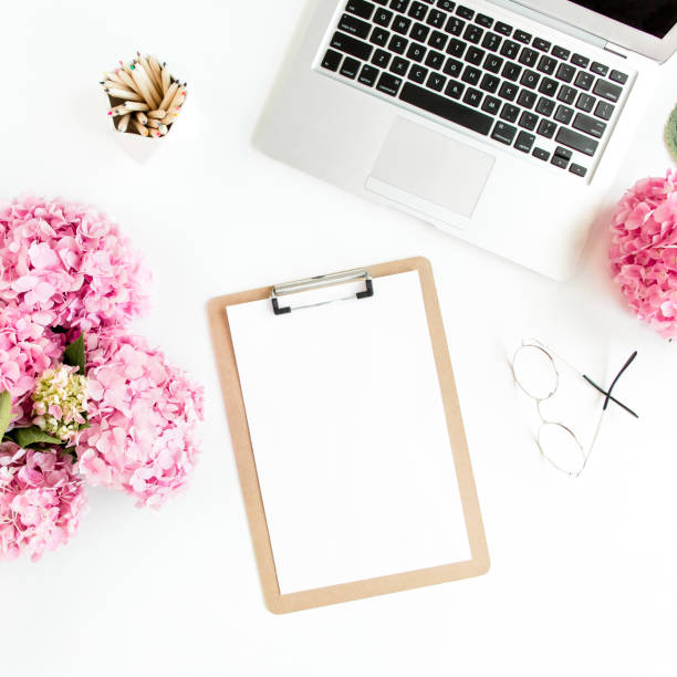 istock Stylized women's desk. Workspace with clipboard, laptop, bouquet hydrangea, accessories on white background. Flat lay. Top view 1270680983