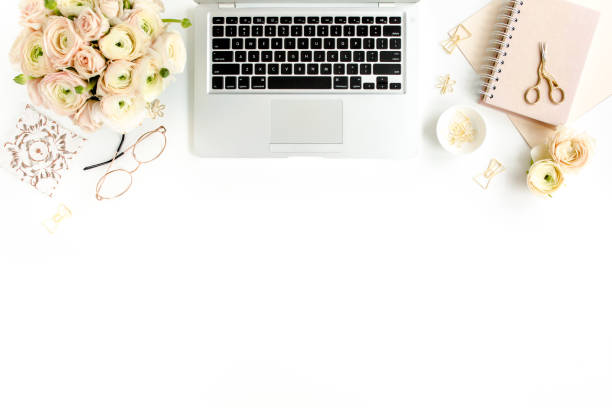 istock Stylized women's home office desk. Workspace with laptop, computer, bouquet ranunculus and roses, clipboard on white background. Flat lay. Top view 1270681017
