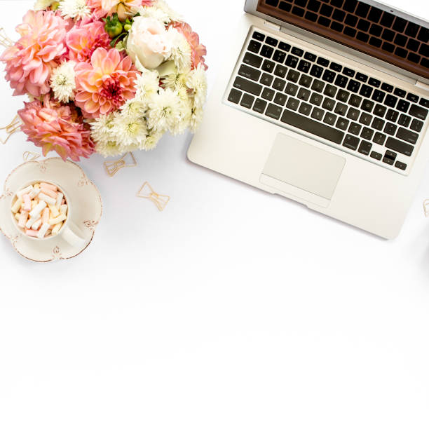 istock Stylized women's home office desk. Workspace with laptop, computer, bouquet ranunculus and roses, clipboard on white background. Flat lay. Top view 1270681044