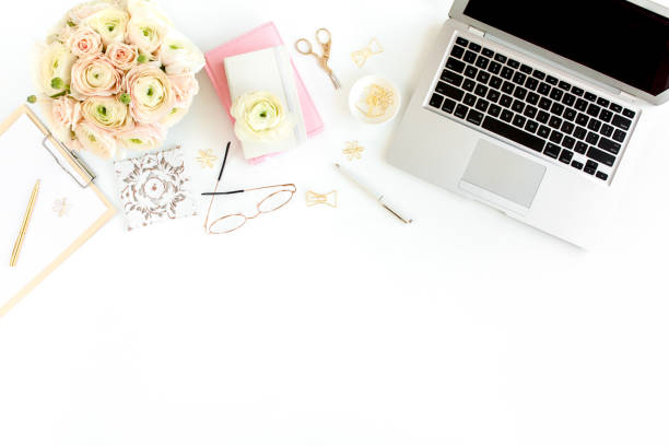 istock Stylized women's home office desk. Workspace with laptop, computer, bouquet ranunculus and roses, clipboard on white background. Flat lay. Top view 1270681755