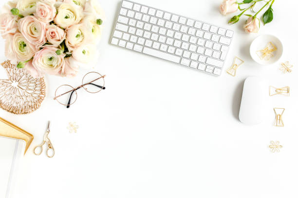 Stylized women's home office desk. Workspace with computer, bouquet ranunculus and roses, clipboard on white background. Flat lay. Top view