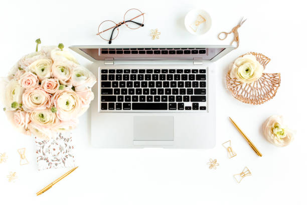 istock Stylized women's home office desk. Workspace with laptop, computer, bouquet ranunculus and roses, clipboard on white background. Flat lay. Top view 1270682038
