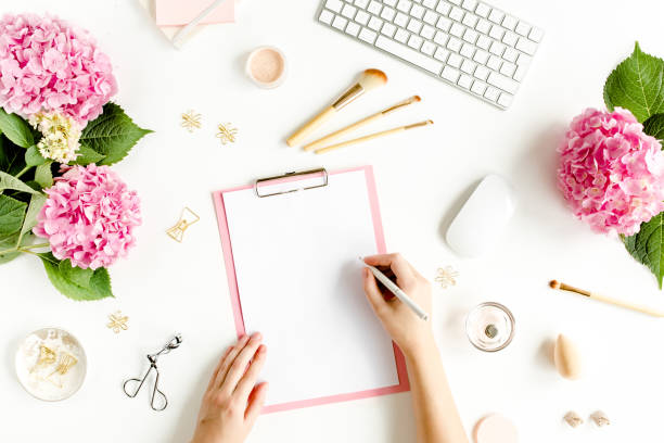 istock Female workspace with female hands, clipboard, bouquet hydrangea, computer, accessories on white background. Stylized women's desk. Flat lay. Top view 1270682354