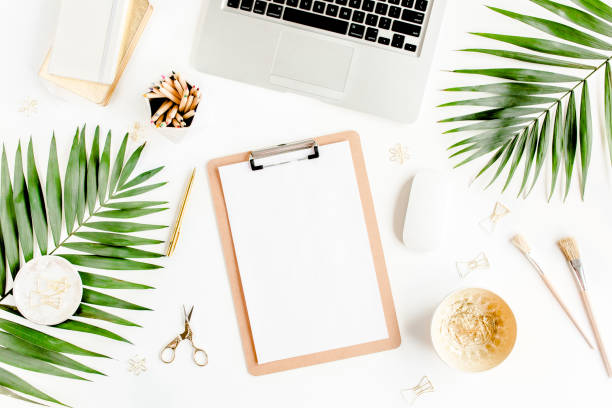 istock Flat lay home office desk. Female workspace with computer, clipboard, tropical palm leaves, accessories on white background. Top view 1270682395