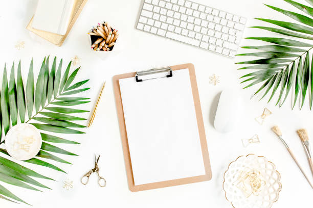 istock Flat lay home office desk. Female workspace with computer, clipboard, tropical palm leaves, accessories on white background. Top view 1270682942