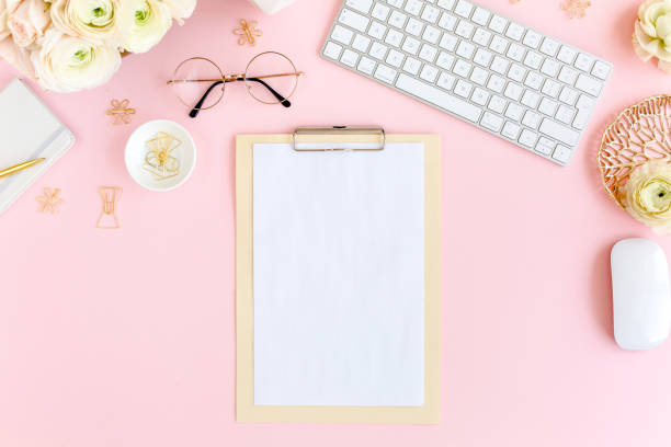 Stylized, pink women's home office desk. Workspace with computer, bouquet ranunculus and roses, clipboard on pink background. Flat lay. Top view