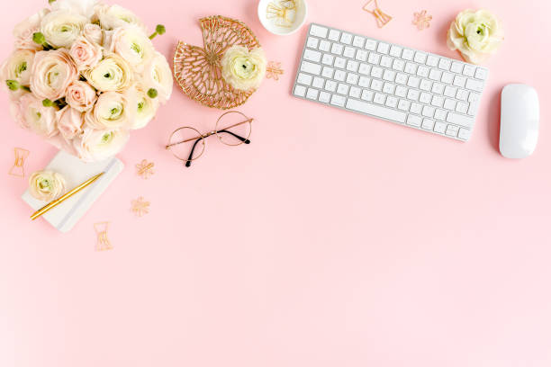 istock Stylized, pink women's home office desk. Workspace with computer, bouquet ranunculus and roses, clipboard on pink background. Flat lay. Top view 1270683416