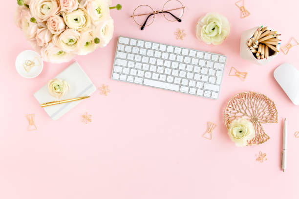 istock Stylized, pink women's home office desk. Workspace with computer, bouquet ranunculus and roses, clipboard on pink background. Flat lay. Top view 1270683544