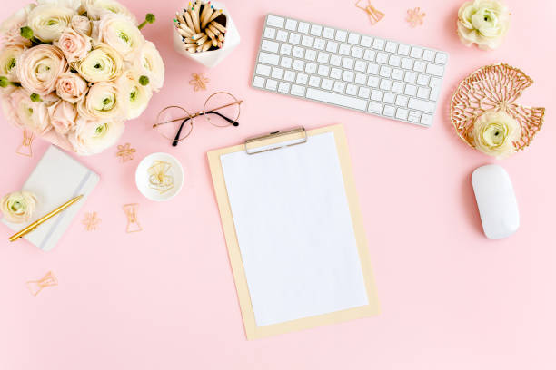 istock Stylized, pink women's home office desk. Workspace with computer, bouquet ranunculus and roses, clipboard on pink background. Flat lay. Top view 1270683582