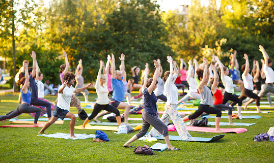 Big group of adults attending a yoga class outside in park.