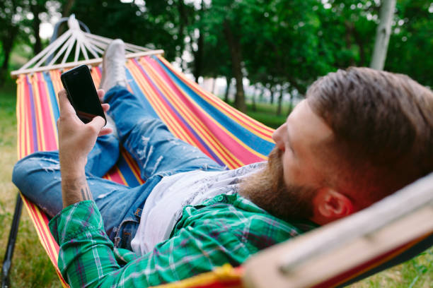 istock man using an app on his mobile phone white swinging in a hammock. 1270685770