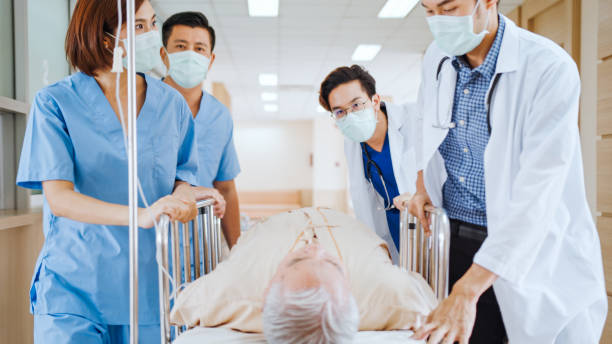Group of Asian emergency doctor and nurse team wear face mask, push emergency stretcher, transport senior patient in hospital. Health care paramedic service, or medical rescue team operation concept grupo de médico de emergencia asiático y equipo de enfermería llevan máscara facial, empujar camilla de emergencia, transportar paciente senior en el hospital. servicio de paramédico de atención médica, o concepto de operación del equipo de rescate