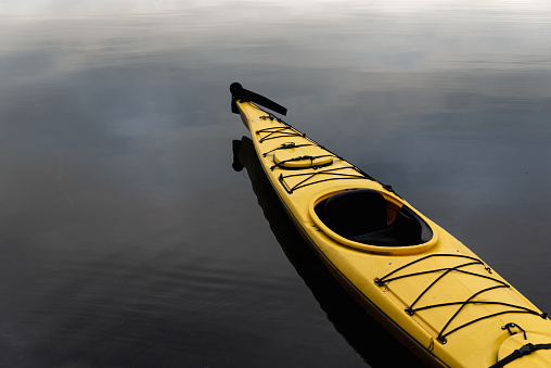 Bright yellow empty ocean kayak resting on calm dark water. in Buck Lake, ON, Canada