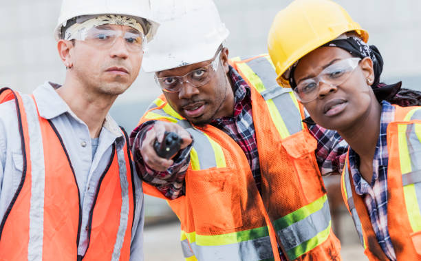 three construction workers in hardhats and safety vests - dirigindo imagens e fotografias de stock