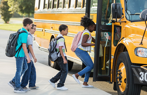 A multi-ethnic group of middle school students, 11 to 13 years old, boarding a yellow school bus.  The boy wearing eyeglasses has down syndrome.