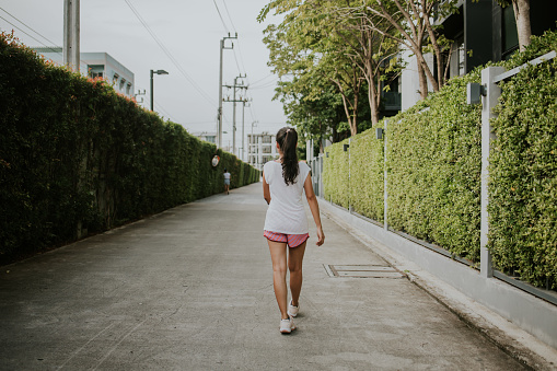 Before jogging, rear view of a young adult woman walking to the street while going to the public park, Bangkok Thailand