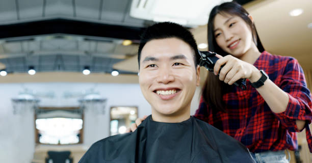 Happy Asian man use the haircut service in Barber shop. Woman hairdresser provide service mind. Hairdressing equipment is clean. End of quarantine and return to open salon hair work stock photo