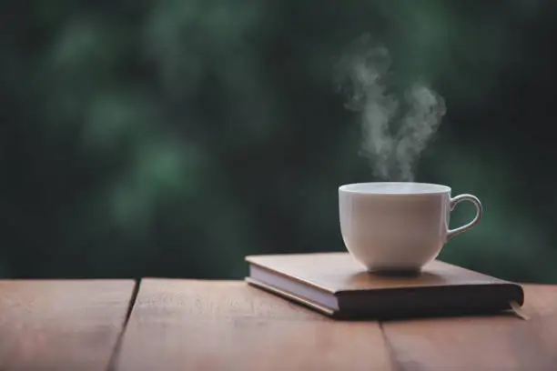 Photo of Hot coffee, smoke, with books for note taking with beautiful nature background.