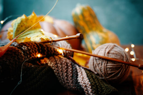 Autumn composition with yarn, wooden needles, lights and pumpkins. Autumn composition with yarn, wooden needles, lights from the garland and colorful pumpkins in the background. Knitting with green and brown yarn. ball of wool photos stock pictures, royalty-free photos & images