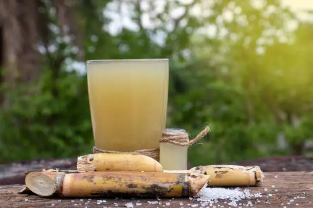 Sugarcane Juice and Sugarcane Pieces in Glass on Wooden Surface with Selective Focus in Horizontal Orientation.