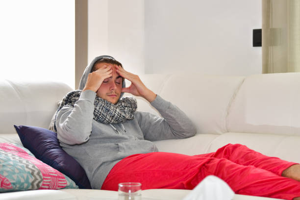 istock Young man looking in pain lying on a sofa while holding his head with both hands. Sickness and healthcare concept. 1270734164