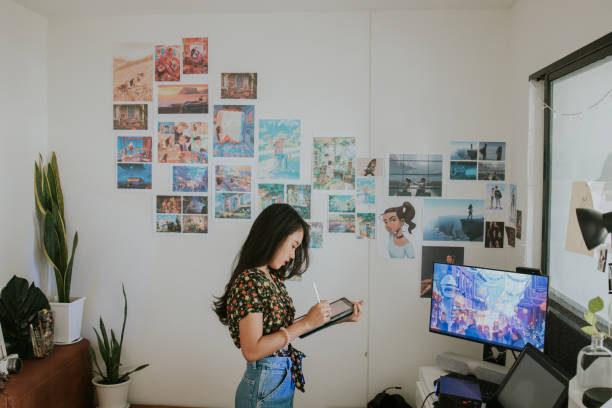Time for preparation. Young creative cartoonist is preparing her portfolio presentation and sketching her work in a digital tablet in front of her master piece work, Bangkok Thailand design occupation stock pictures, royalty-free photos & images